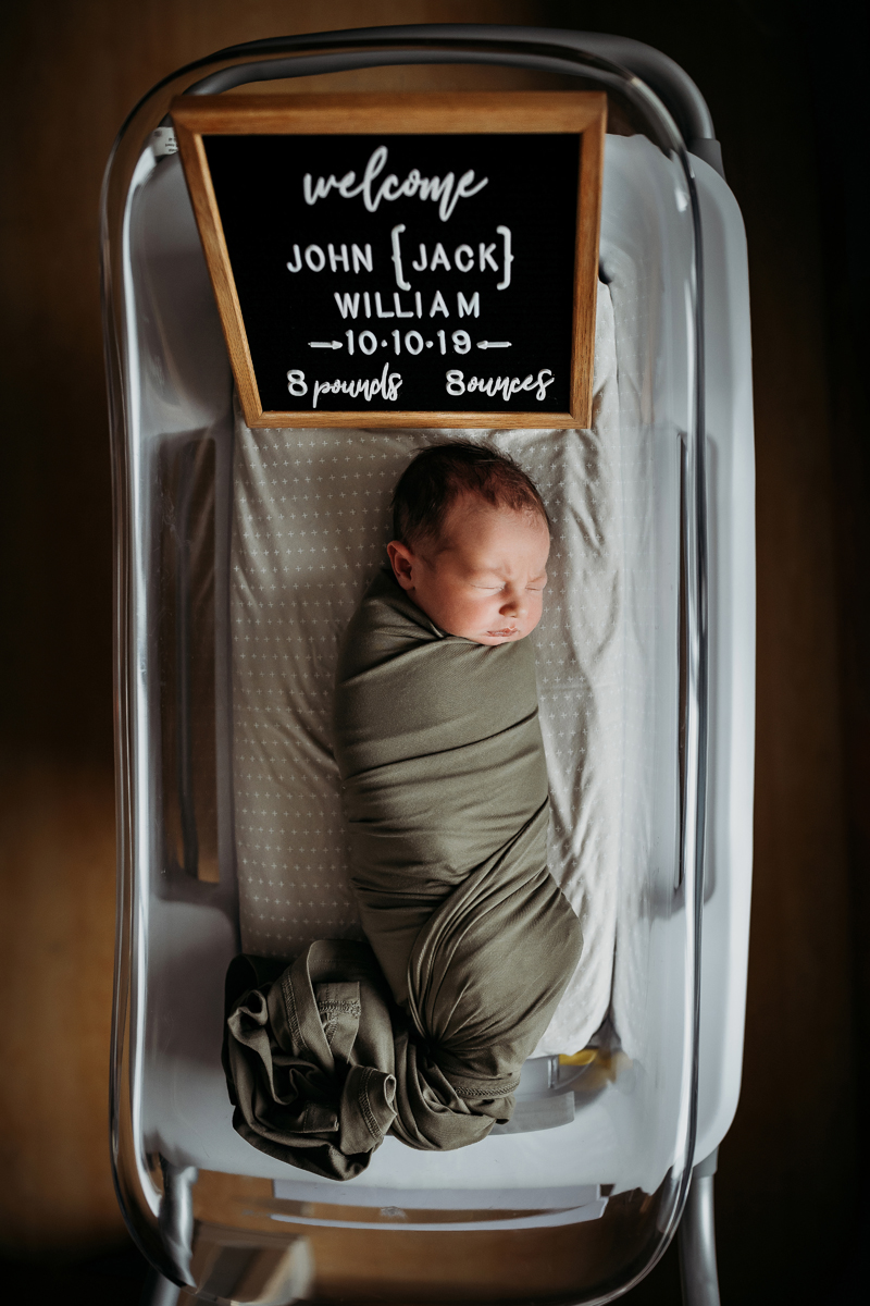 Fresh 48 Photography, a baby lays swaddled in a olive colored blanket in a hospital criP