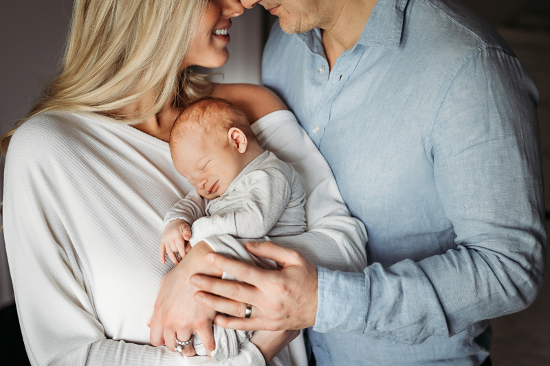 Newborn Photography, dad leans into mom as they both hold tight their newborn baby